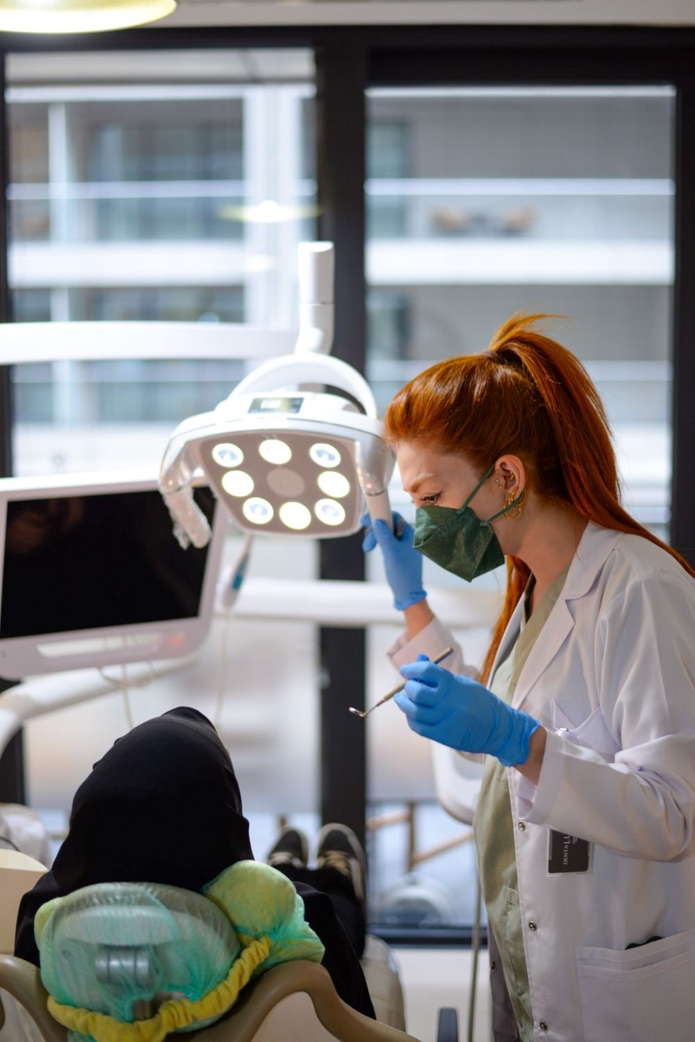 Chirurgienne-dentiste en blouse blanche et masque soignant une patiente sous la lampe du cabinet dentaire