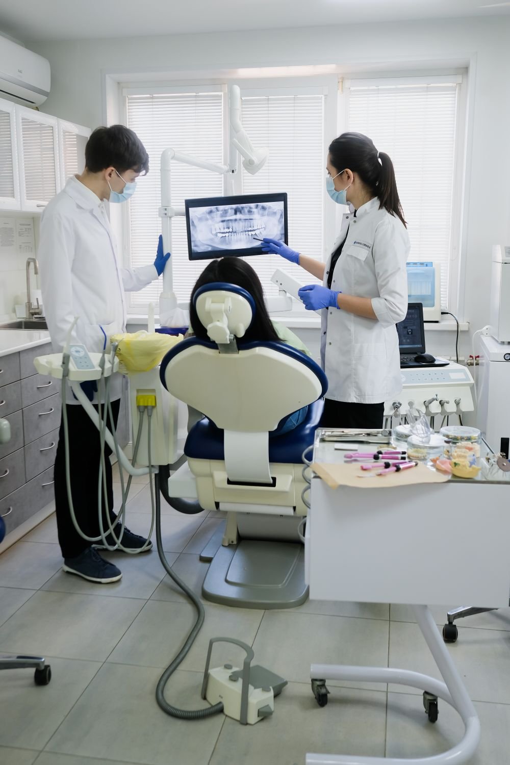 Deux chirurgiens-dentistes examinent une radiographie panoramique sur écran avec une patiente installée au fauteuil